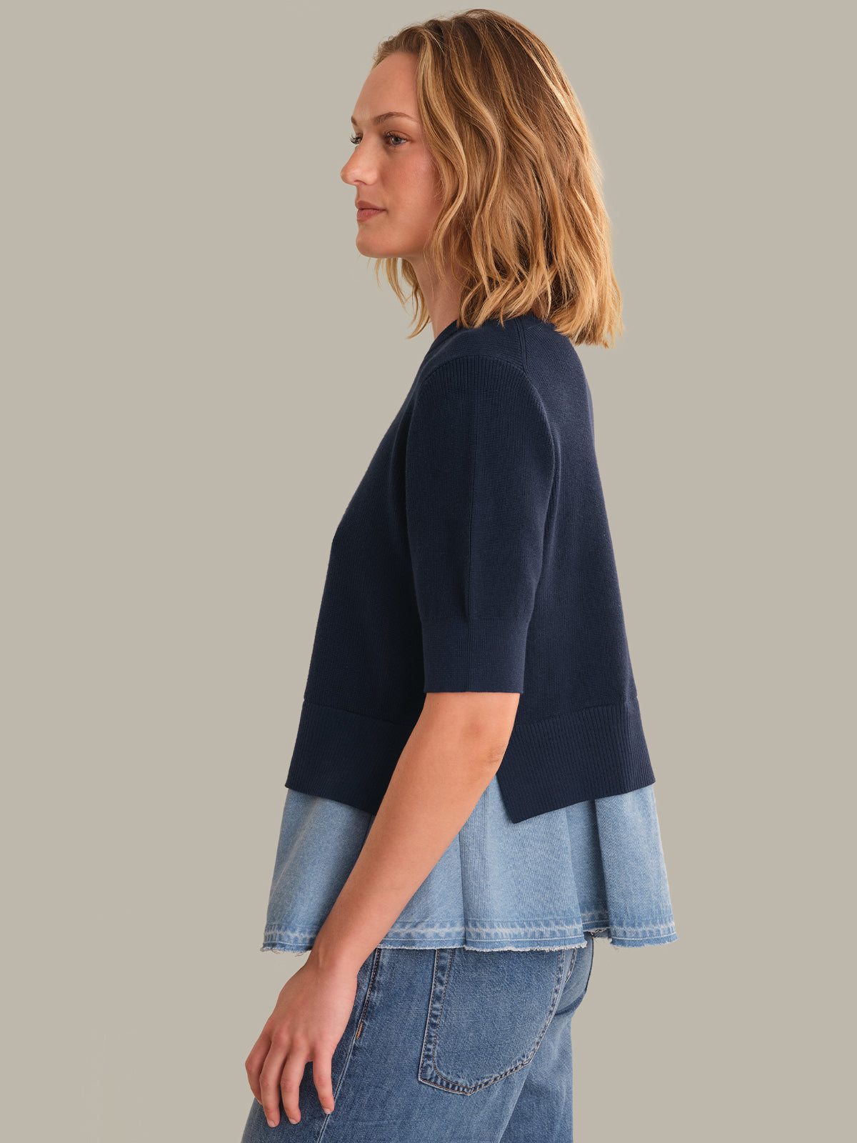 Woman wearing a navy top over a denim skirt on a plain background