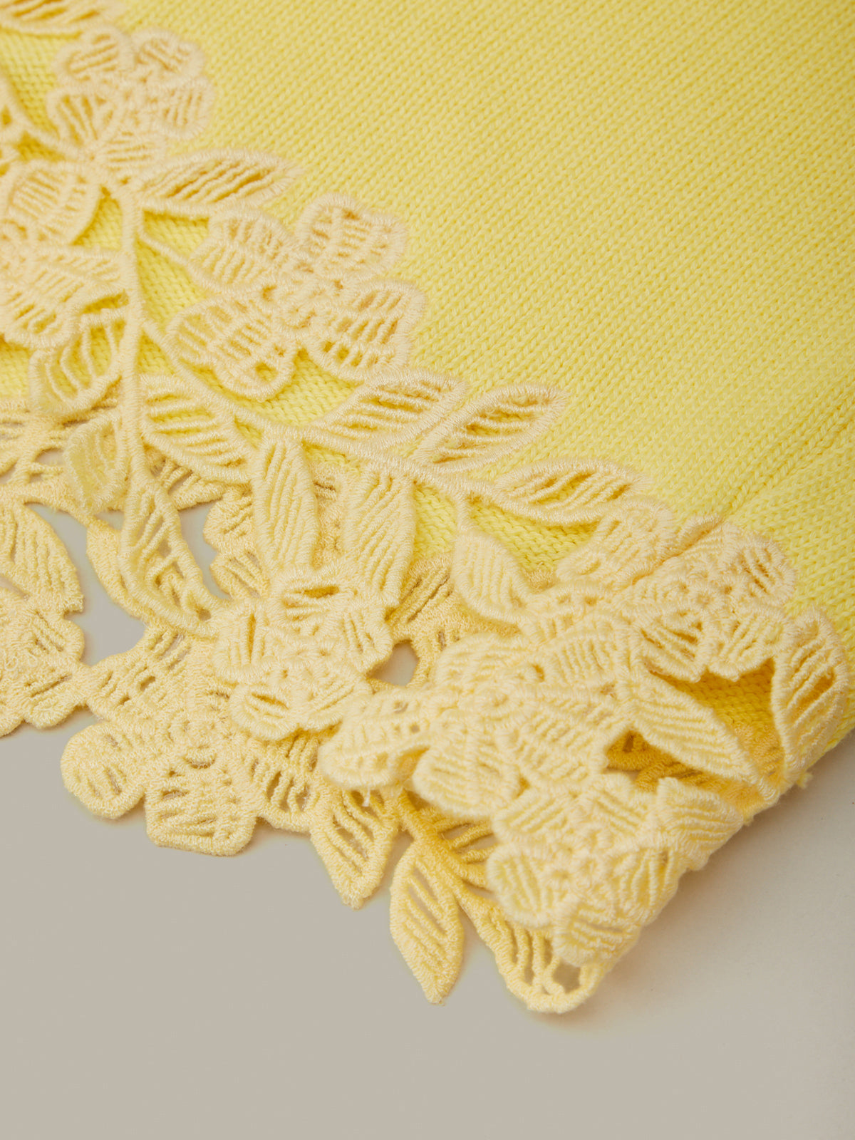 Yellow fabric with intricate lace detailing on a neutral background
