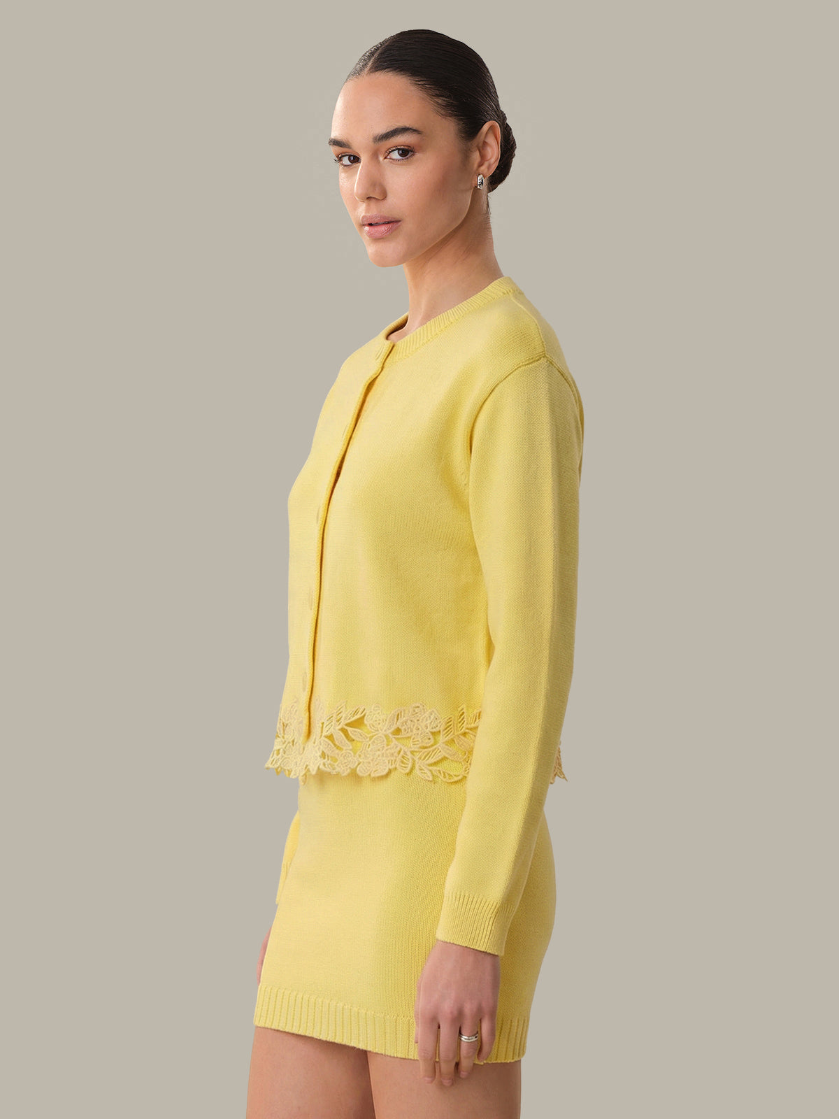 Woman wearing a yellow suit with lace details on a plain background