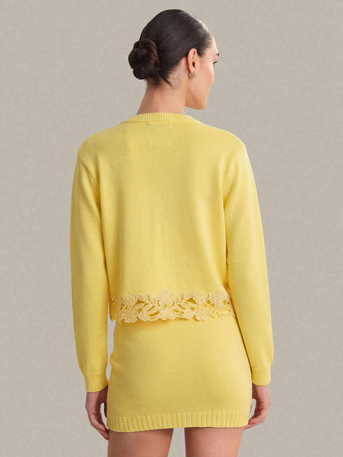 Woman wearing a yellow sweater with lace trim on a plain background
