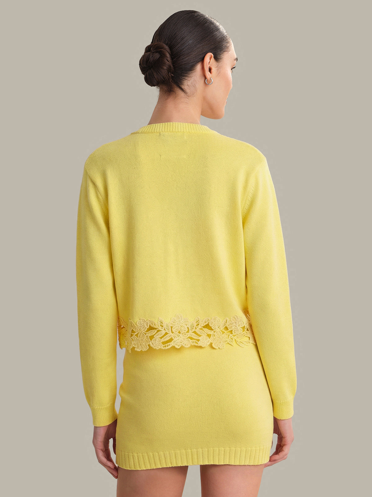 Woman wearing a yellow sweater with lace trim on a plain background