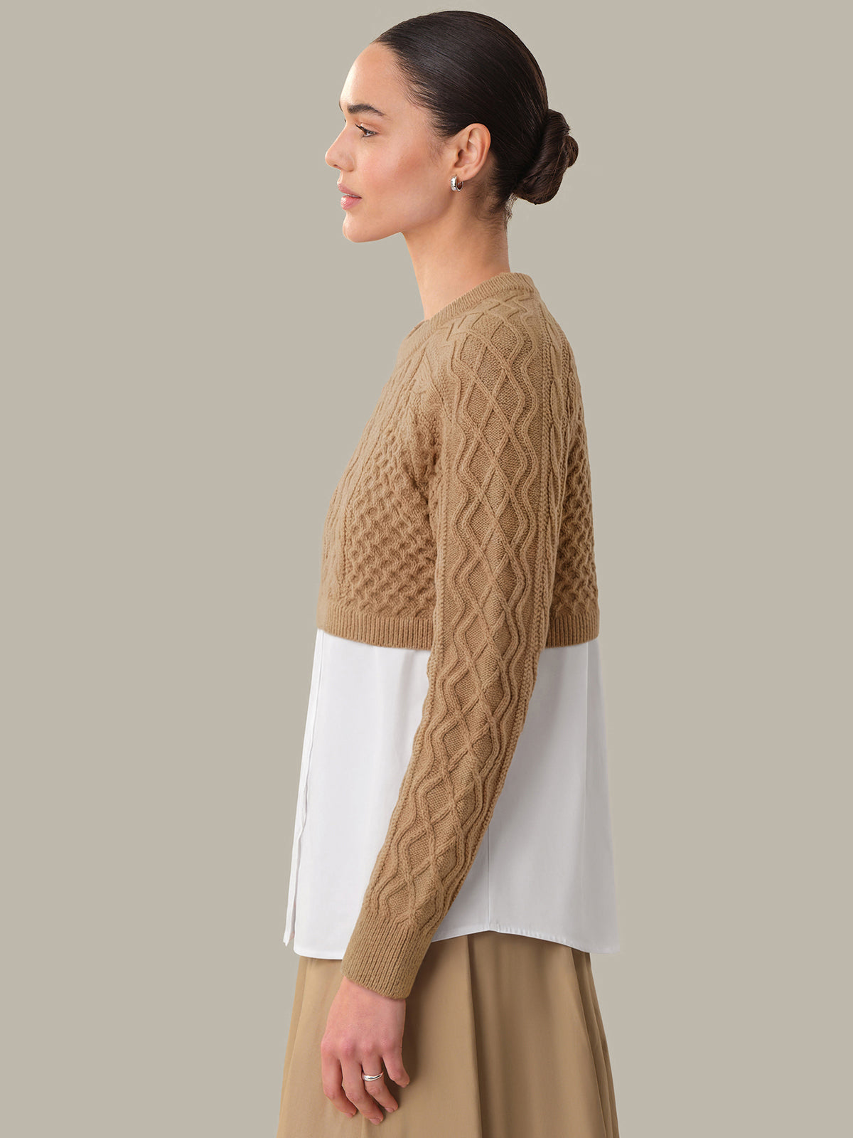 Woman wearing a brown cable knit sweater over a white shirt on a beige background
