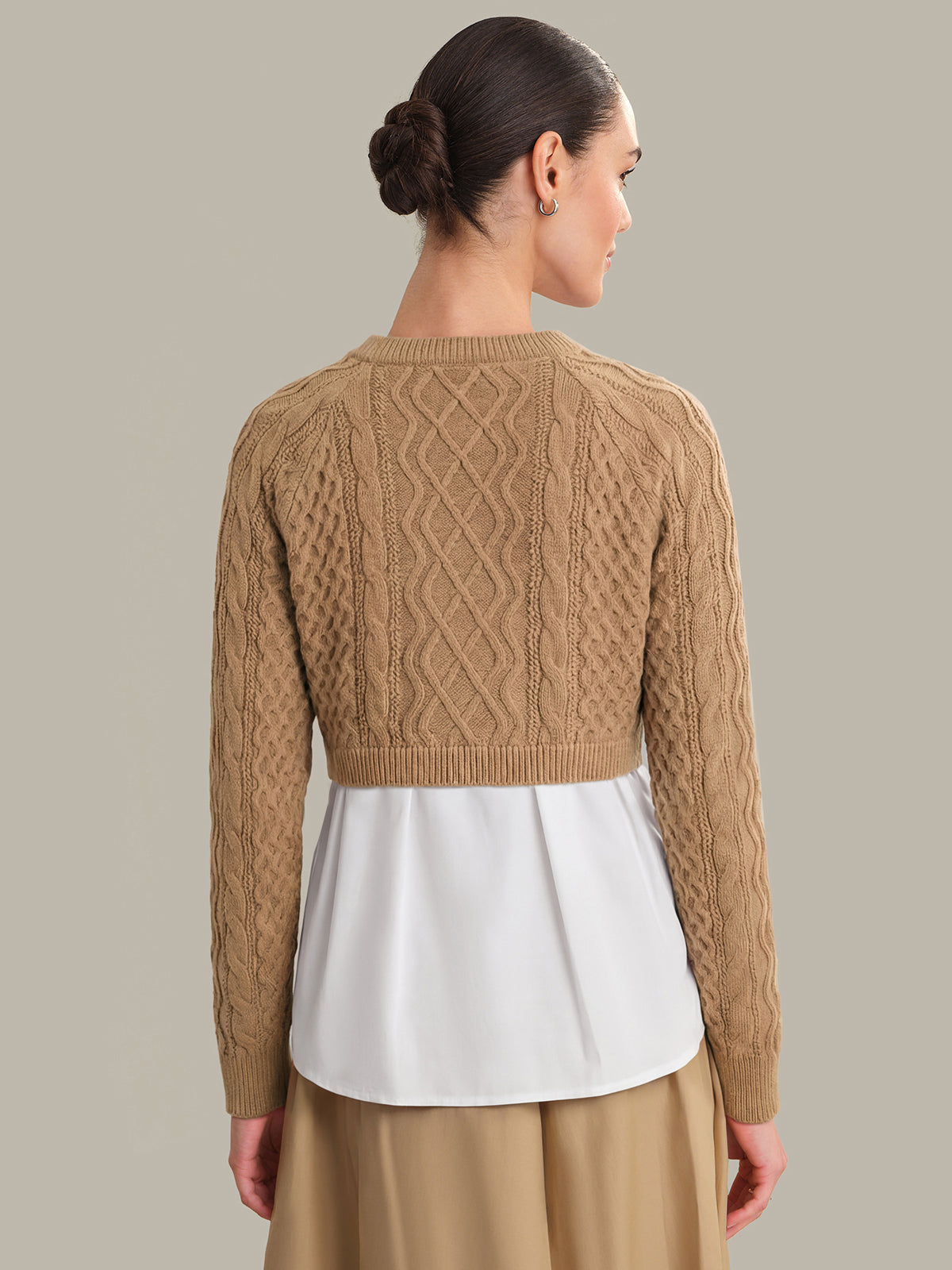 Woman wearing a brown cable knit sweater over a white shirt on a beige background