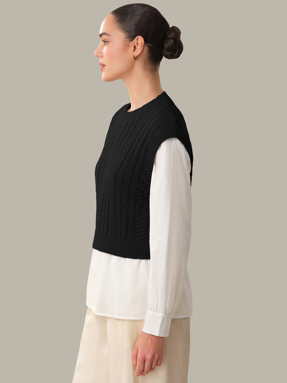 Woman wearing a black knitted vest over a white shirt on a neutral background
