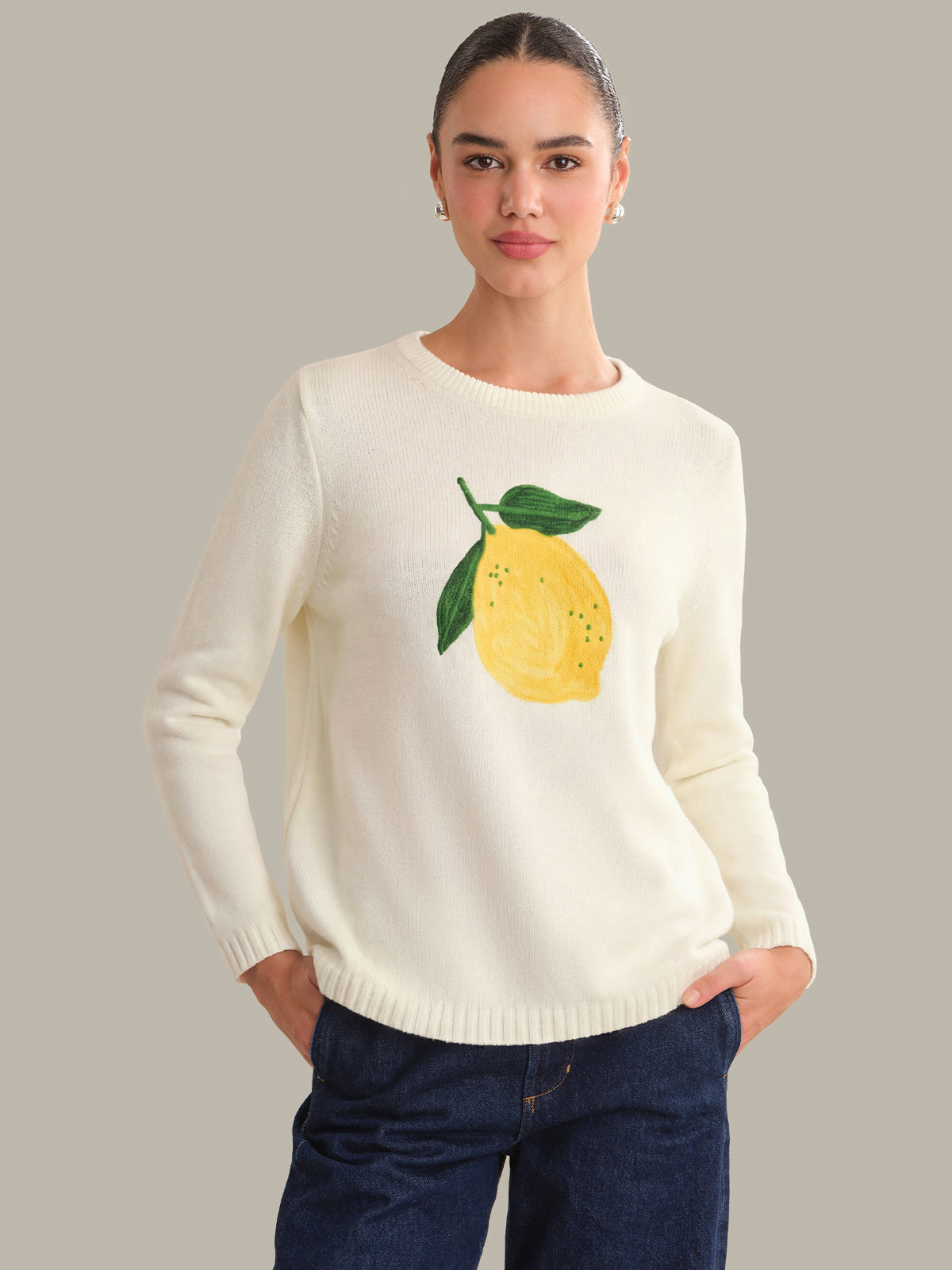 Woman wearing a cream sweater with a lemon design on a gray background