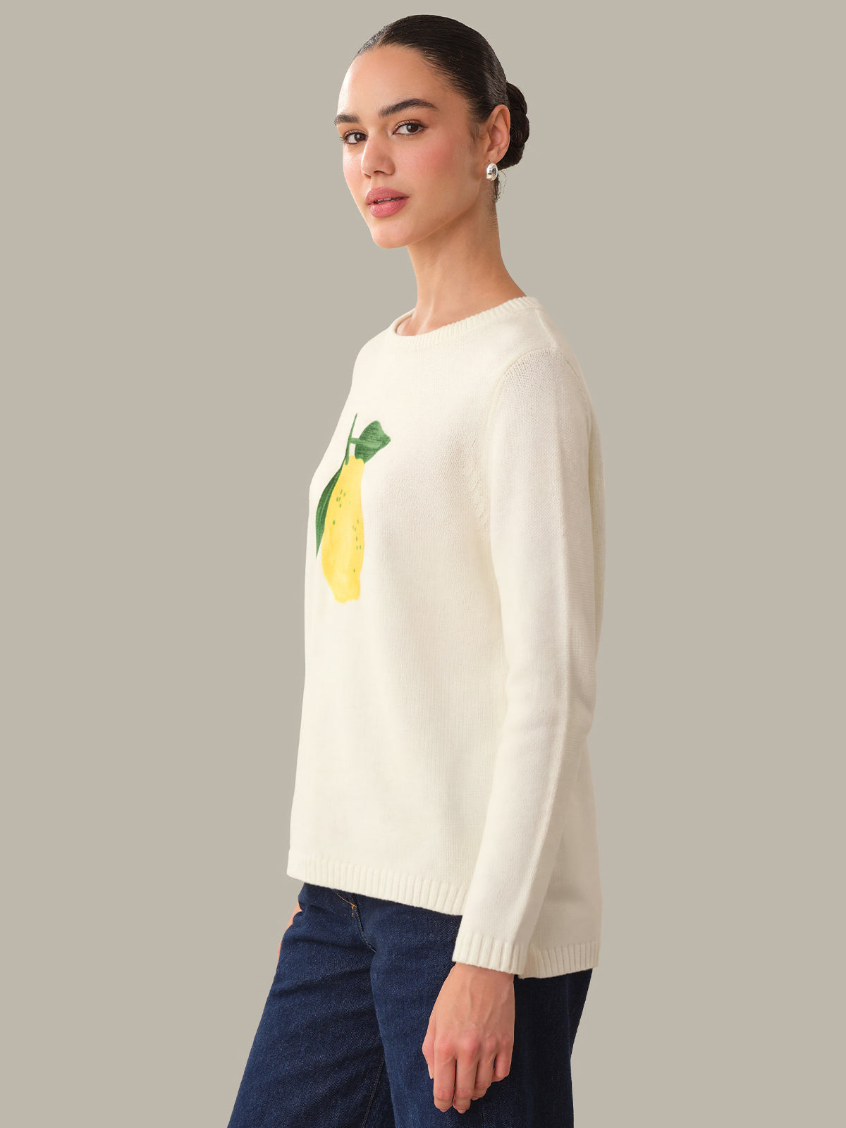 Woman wearing a cream sweater with a lemon design on a plain background