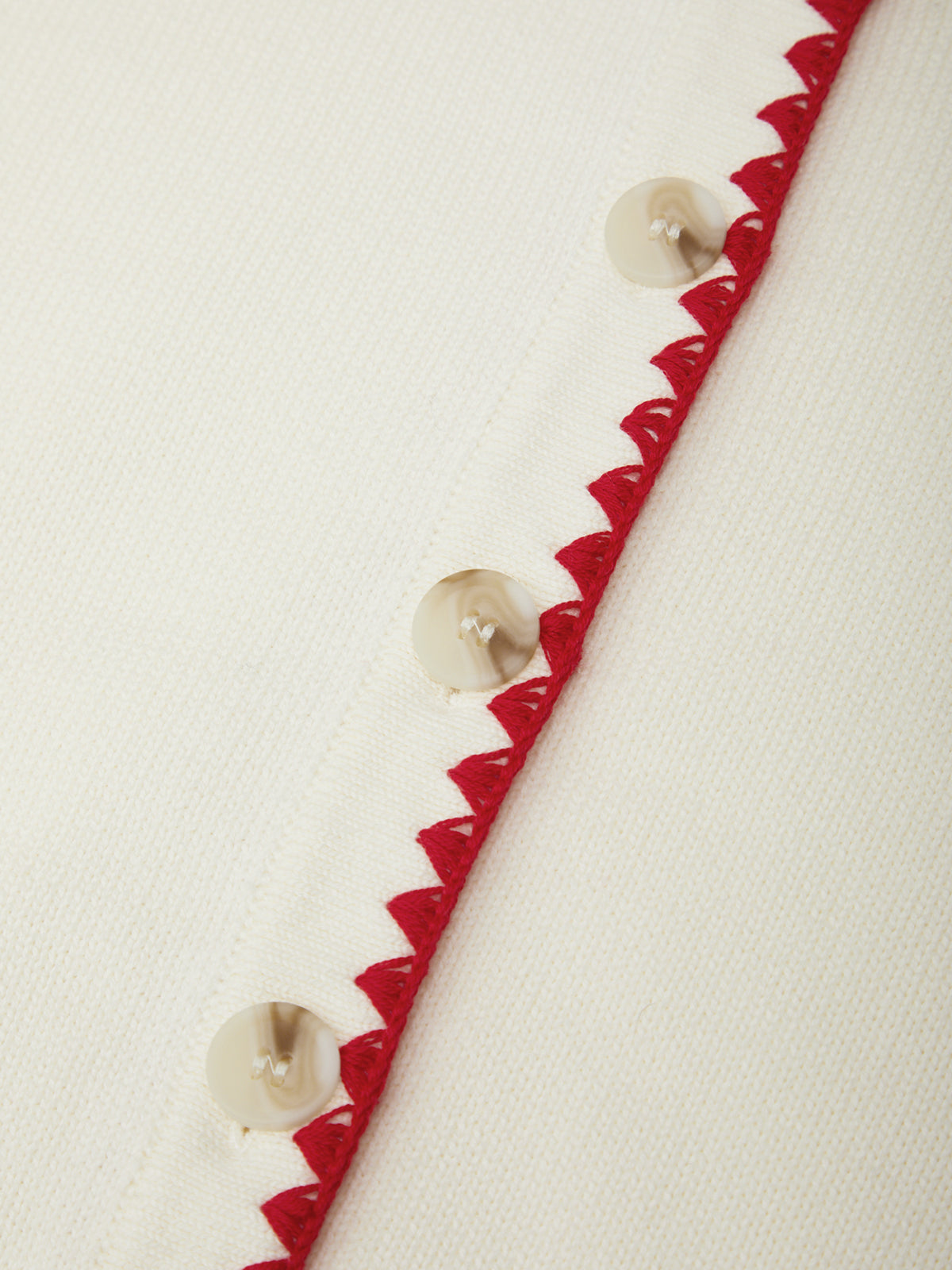 Close-up of a decorative trim with red zigzag pattern and pearl-like beads on a white background
