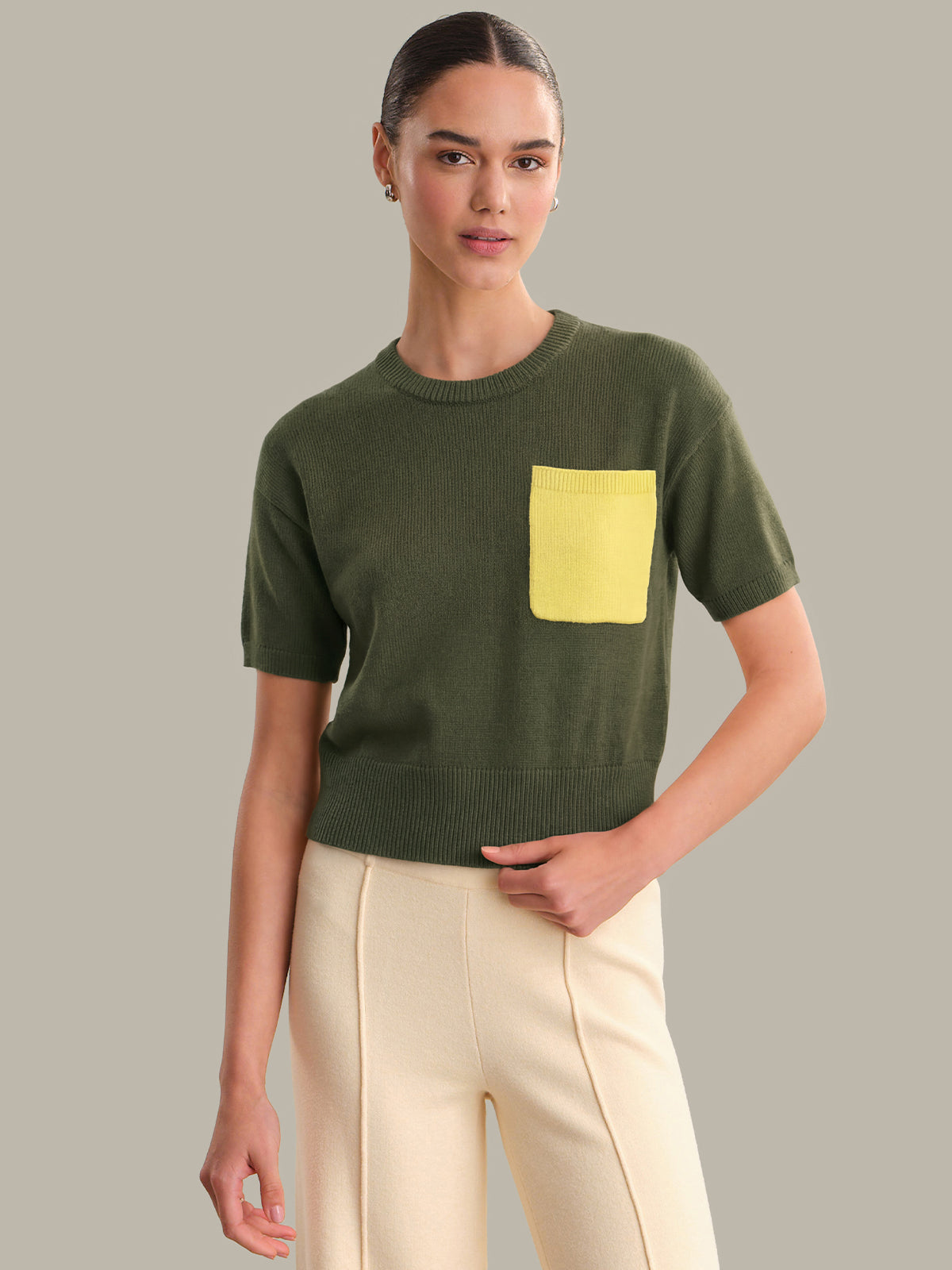 Woman wearing a green sweater with a yellow pocket against a gray background