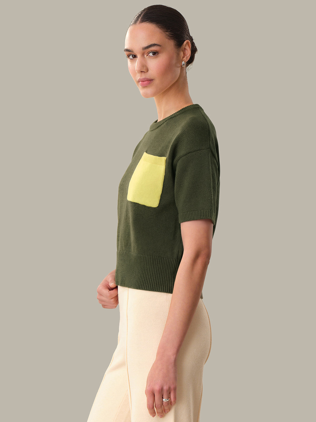 Woman wearing a green sweater with a yellow pocket against a gray background
