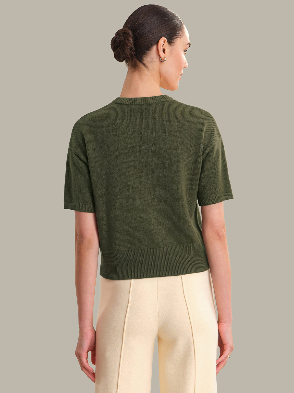 Woman wearing a green sweater and beige pants against a neutral background