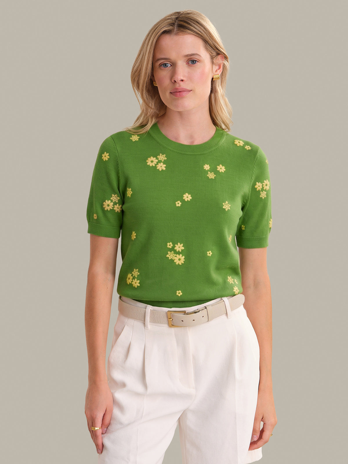 Woman wearing a green sweater with yellow floral patterns on a plain background