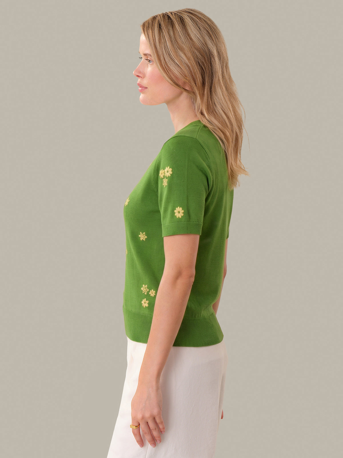 Woman wearing a green sweater with yellow floral patterns on a plain background