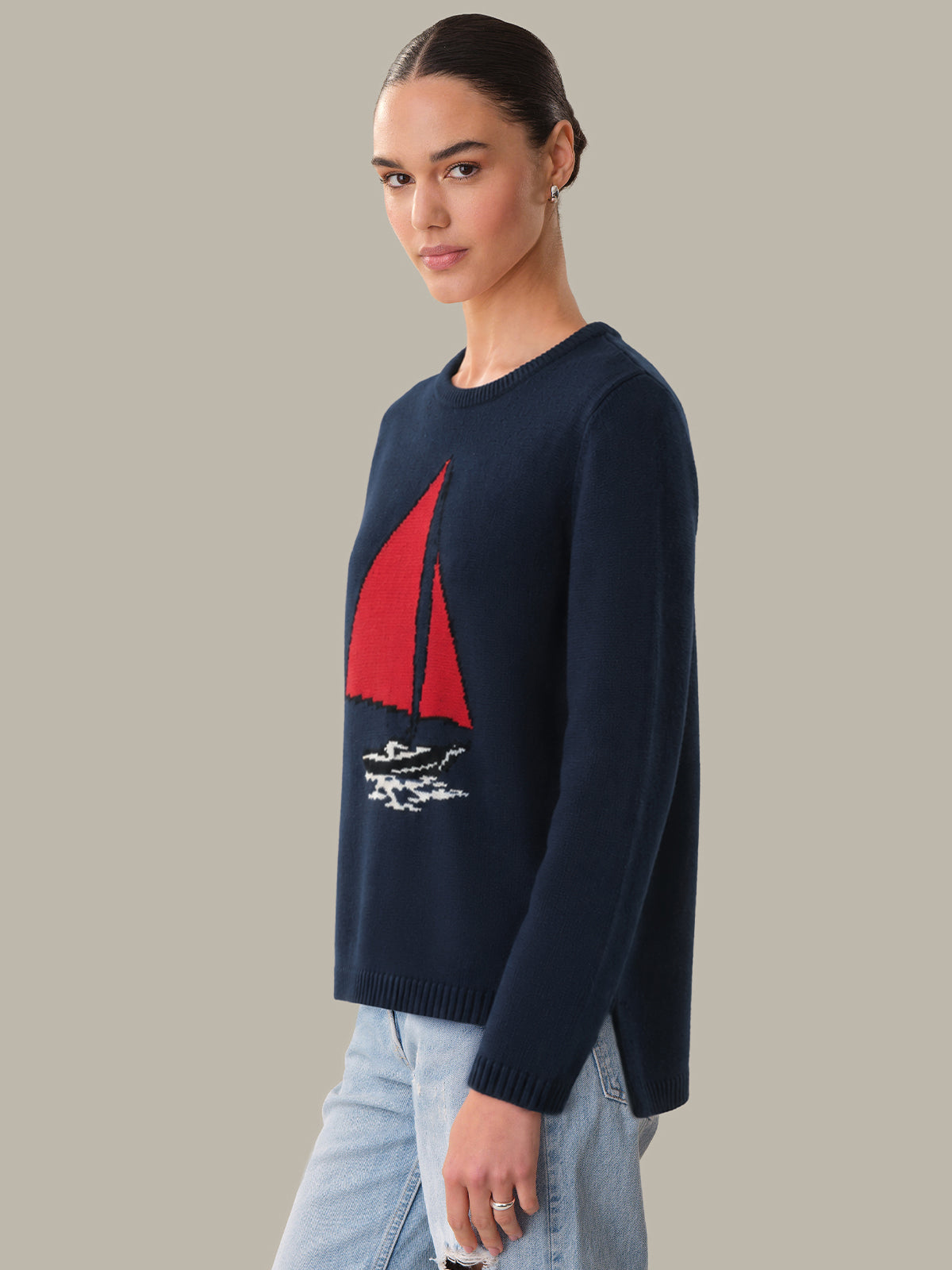 Person wearing a navy sweater with a red sailboat design on a plain background