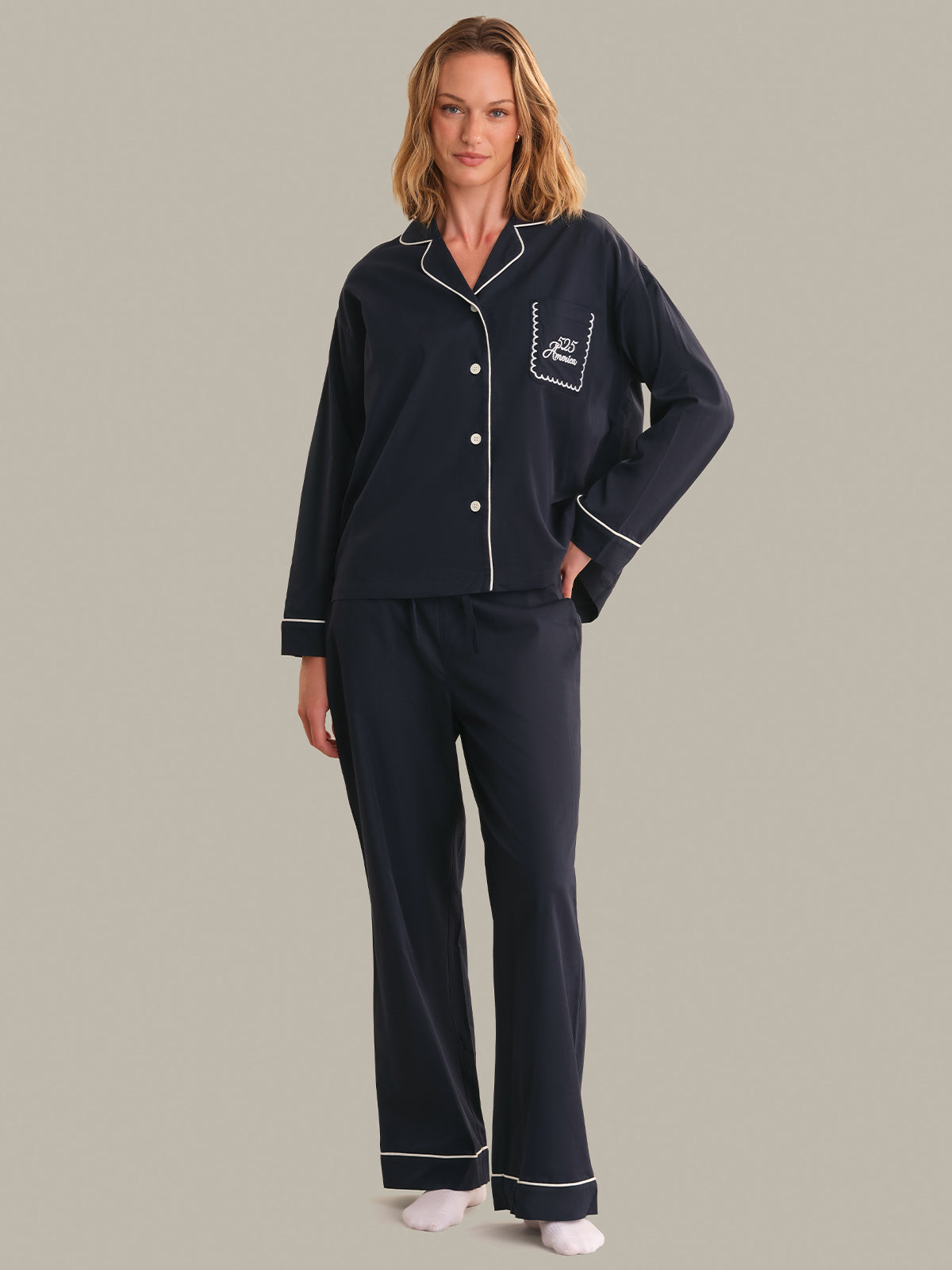 Woman wearing navy pajamas with white piping on a gray background