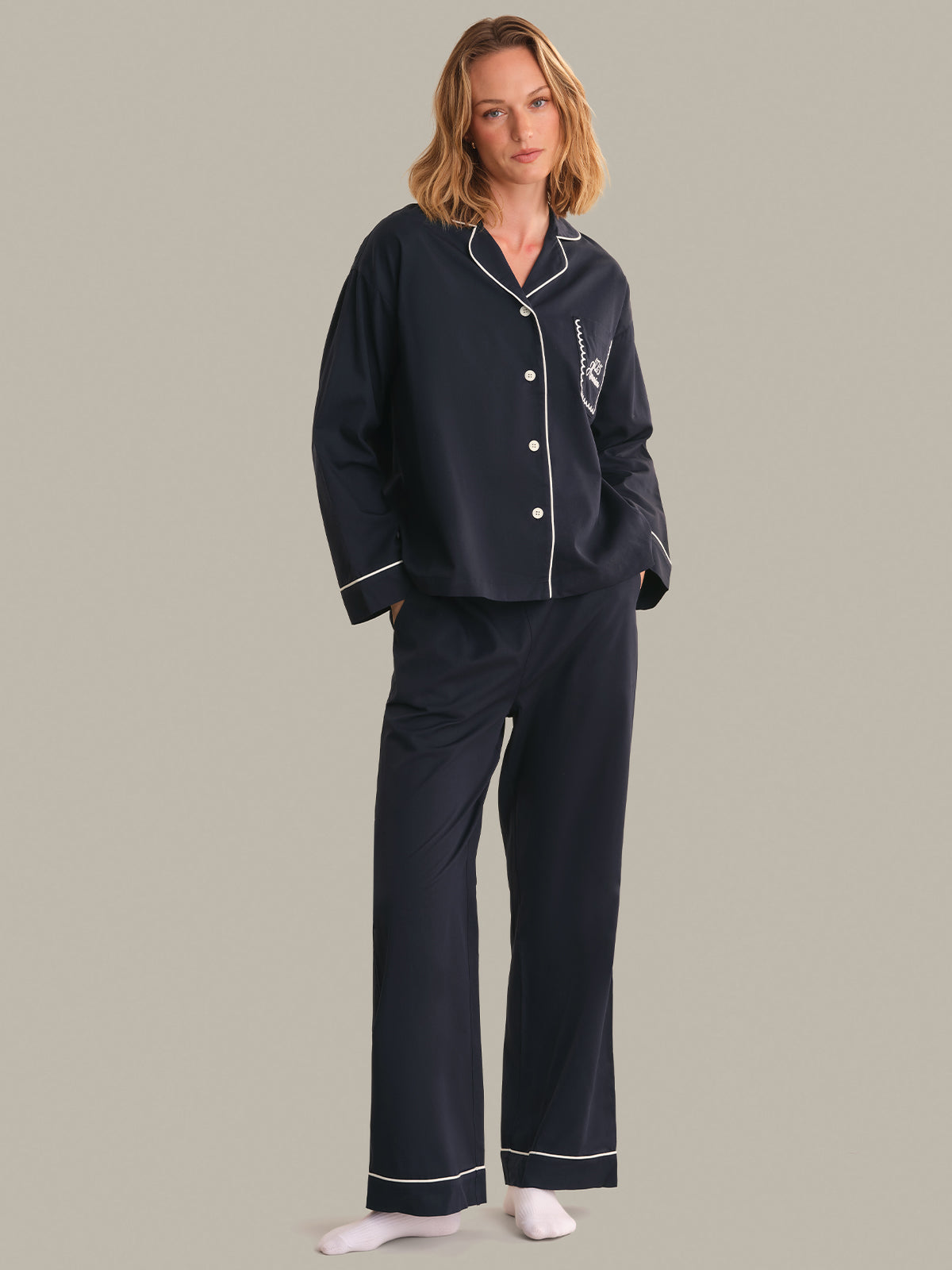 Woman wearing navy pajamas with white piping on a gray background
