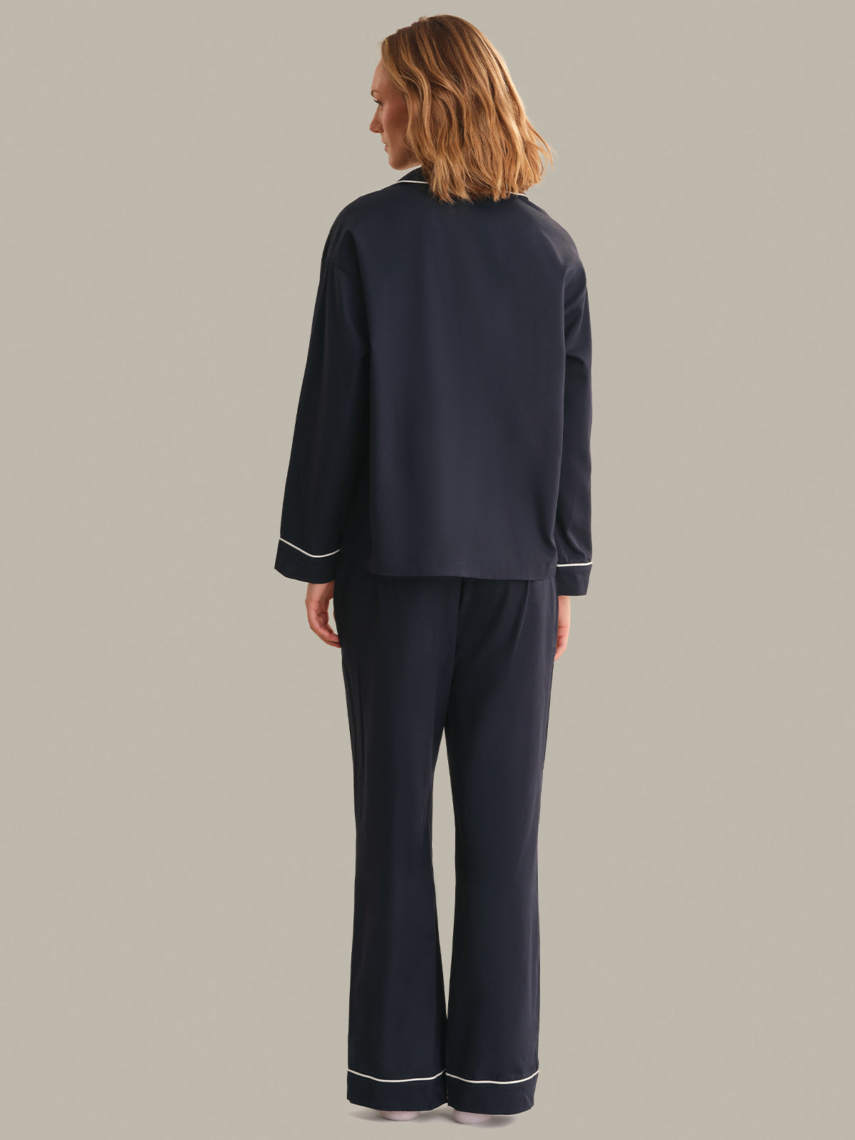 Person wearing a navy pajama set with white piping on a gray background