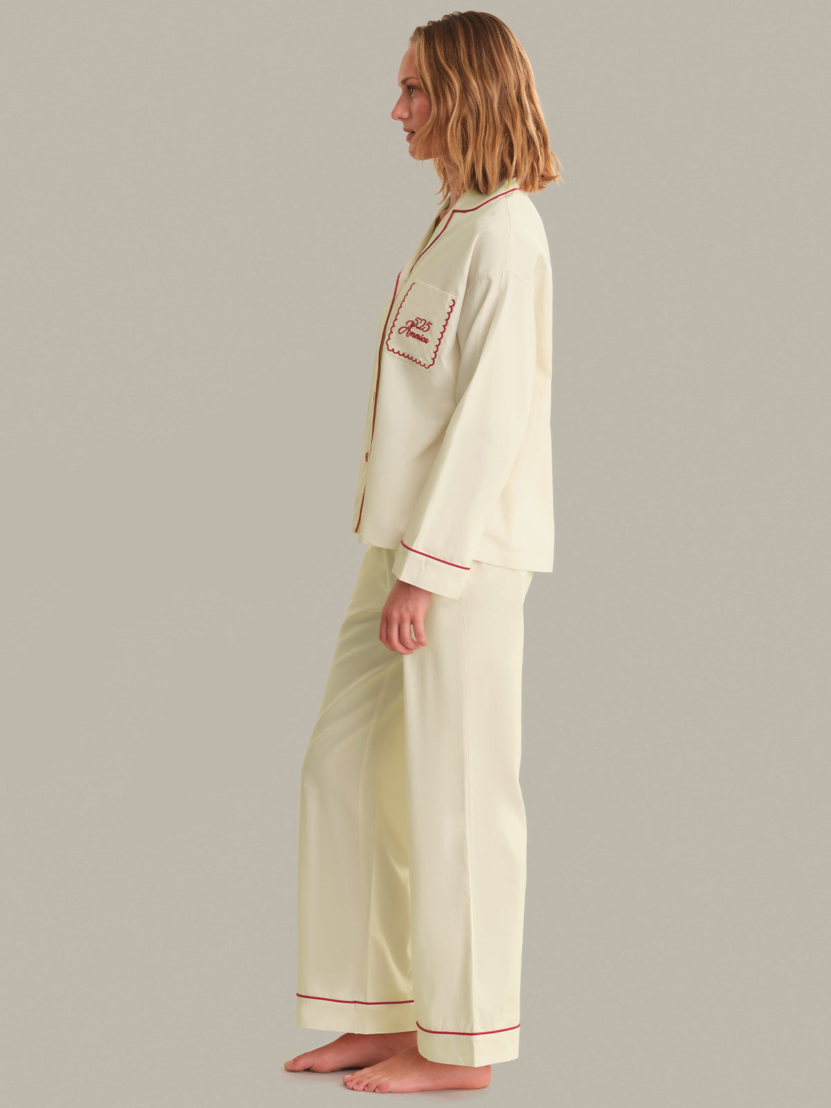 Person wearing a cream-colored pajama set with red trim on a gray background