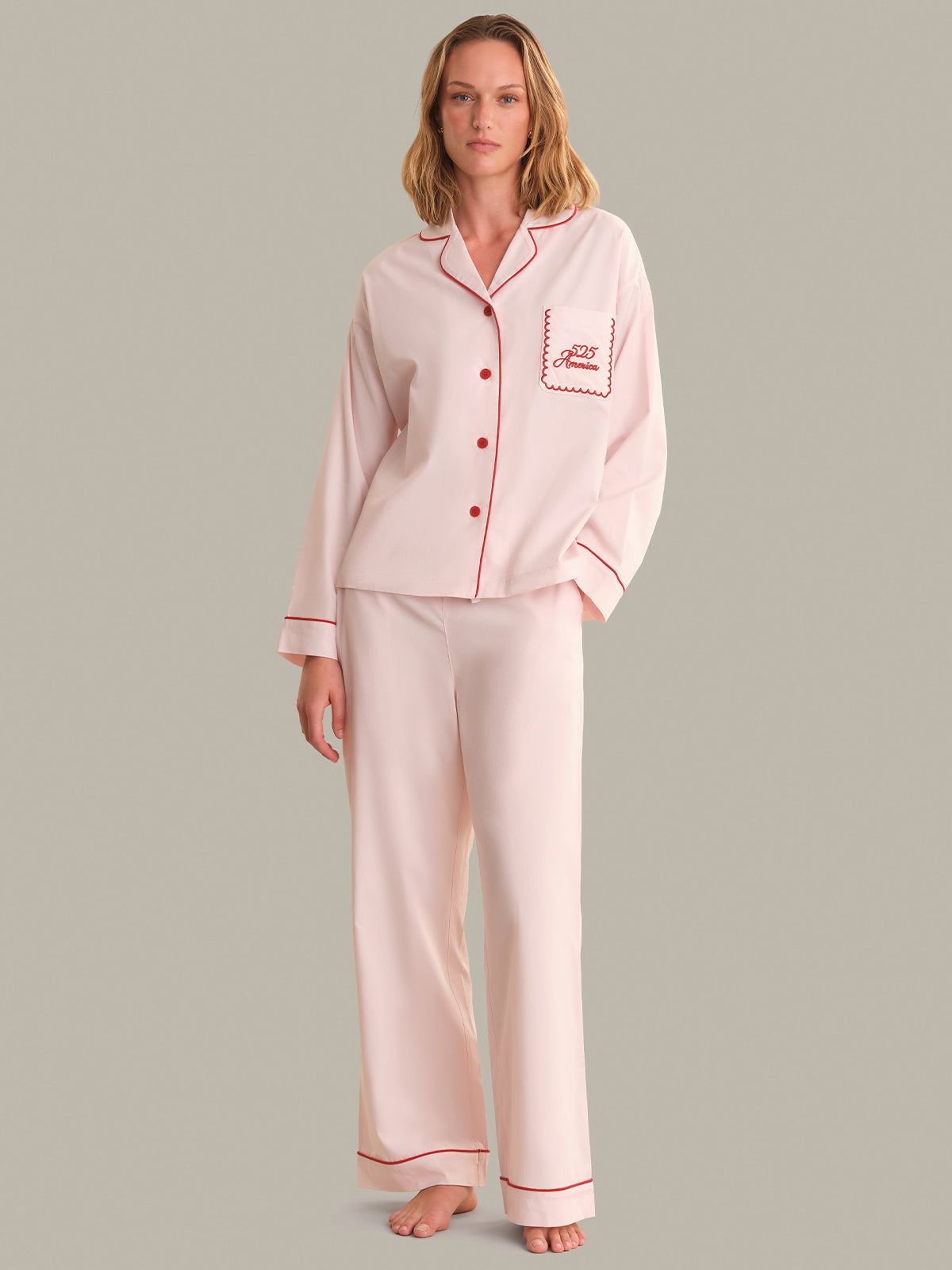 Woman wearing a pink pajama set with red piping on a gray background