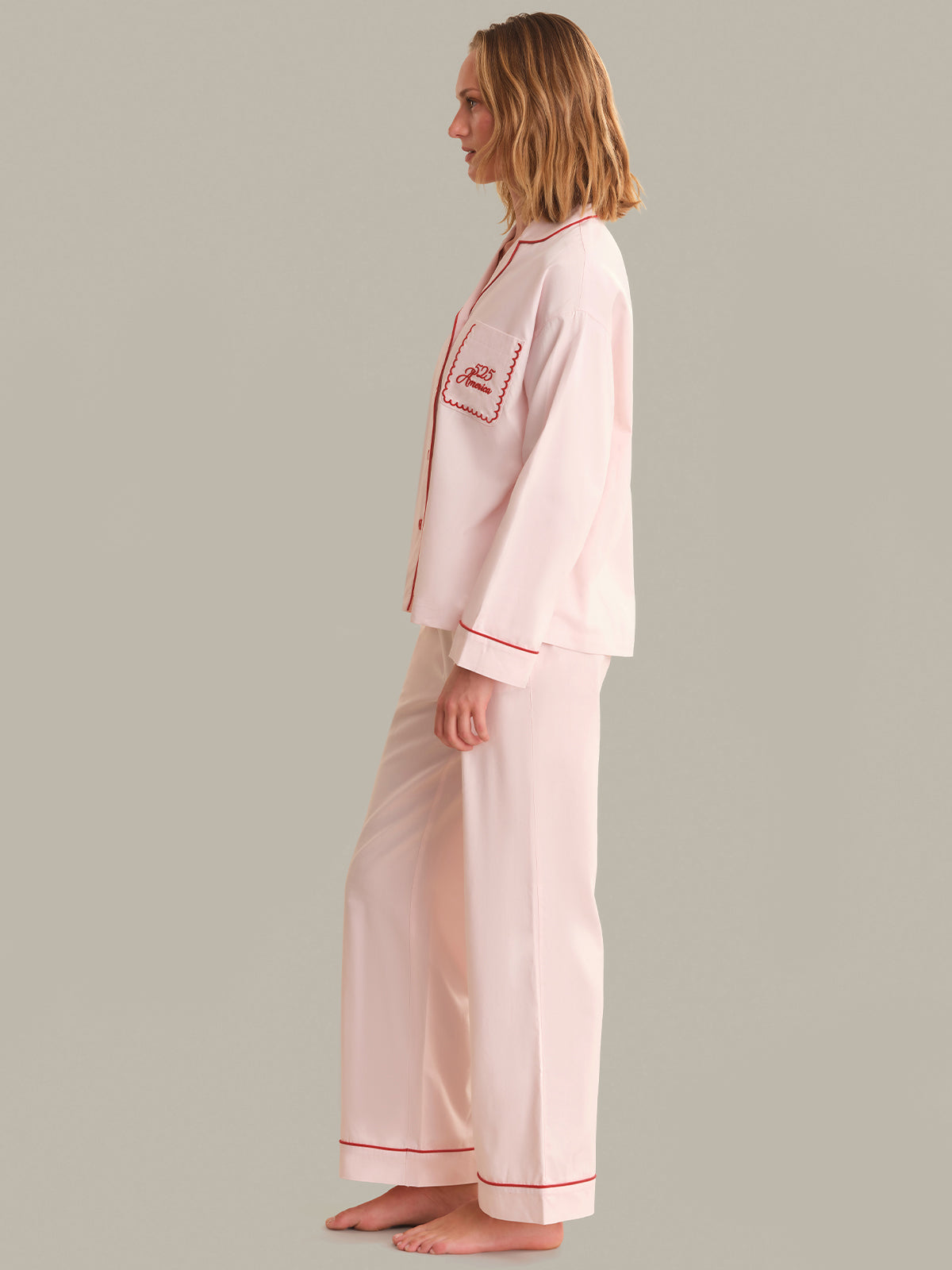 Person wearing a light pink pajama set with red piping on a gray background