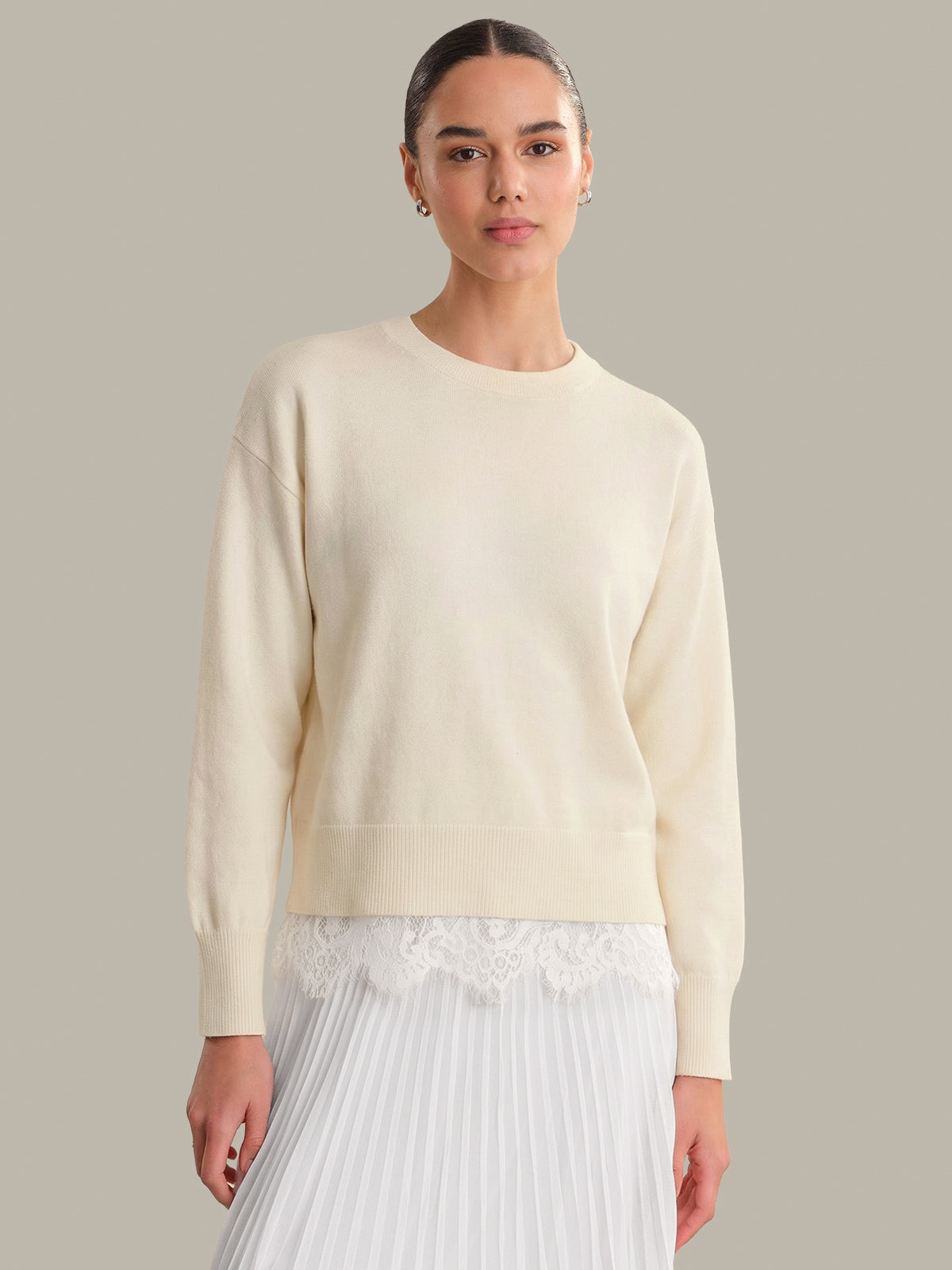 Woman wearing a light-colored sweater and white pants against a neutral background