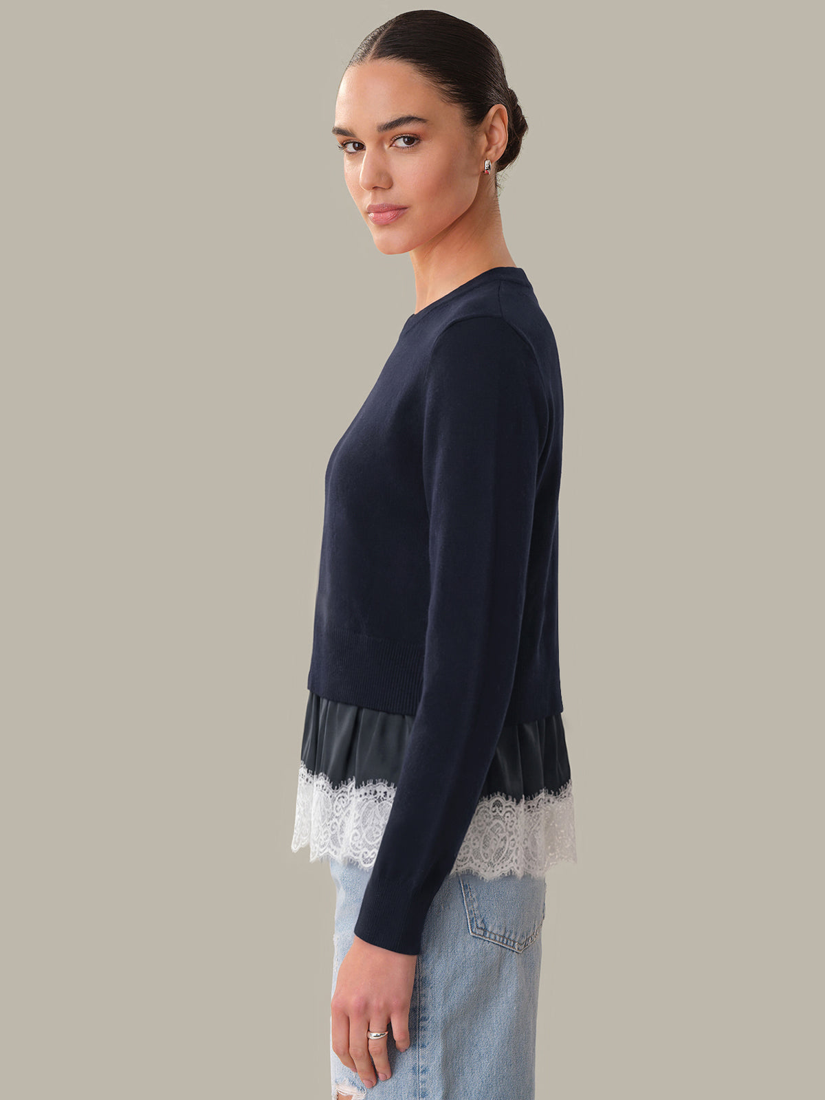 Woman wearing a navy sweater with lace trim on a neutral background