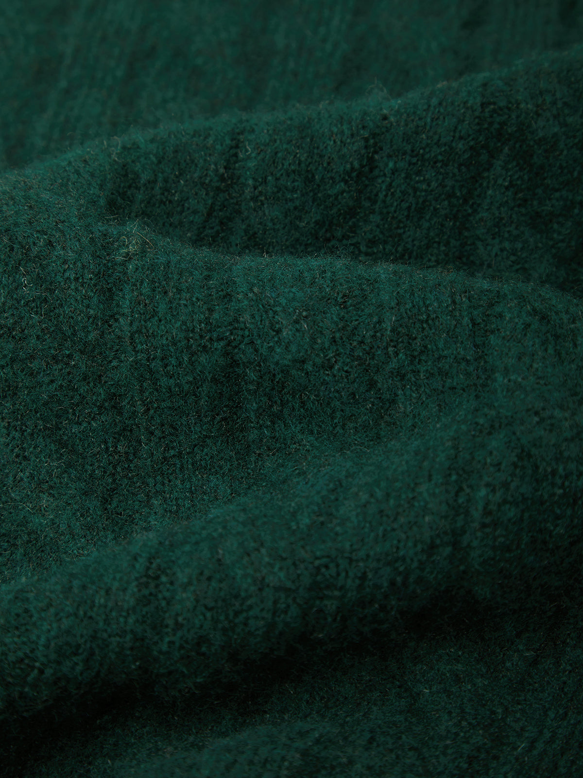 A close-up of dark forest green textured knit fabric with soft folds and ribbed detailing.
