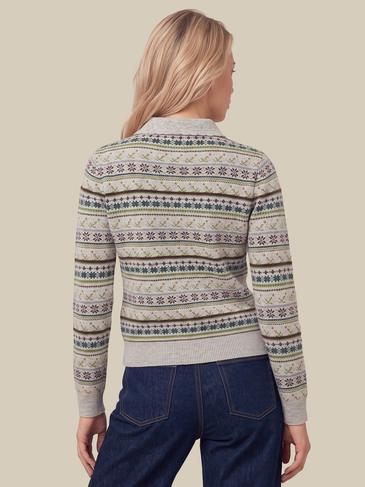 A woman viewed from the back wearing a cropped knit sweater with horizontal Fair Isle style patterns in beige, brown, green, and purple, paired with dark blue jeans, against a solid beige background.