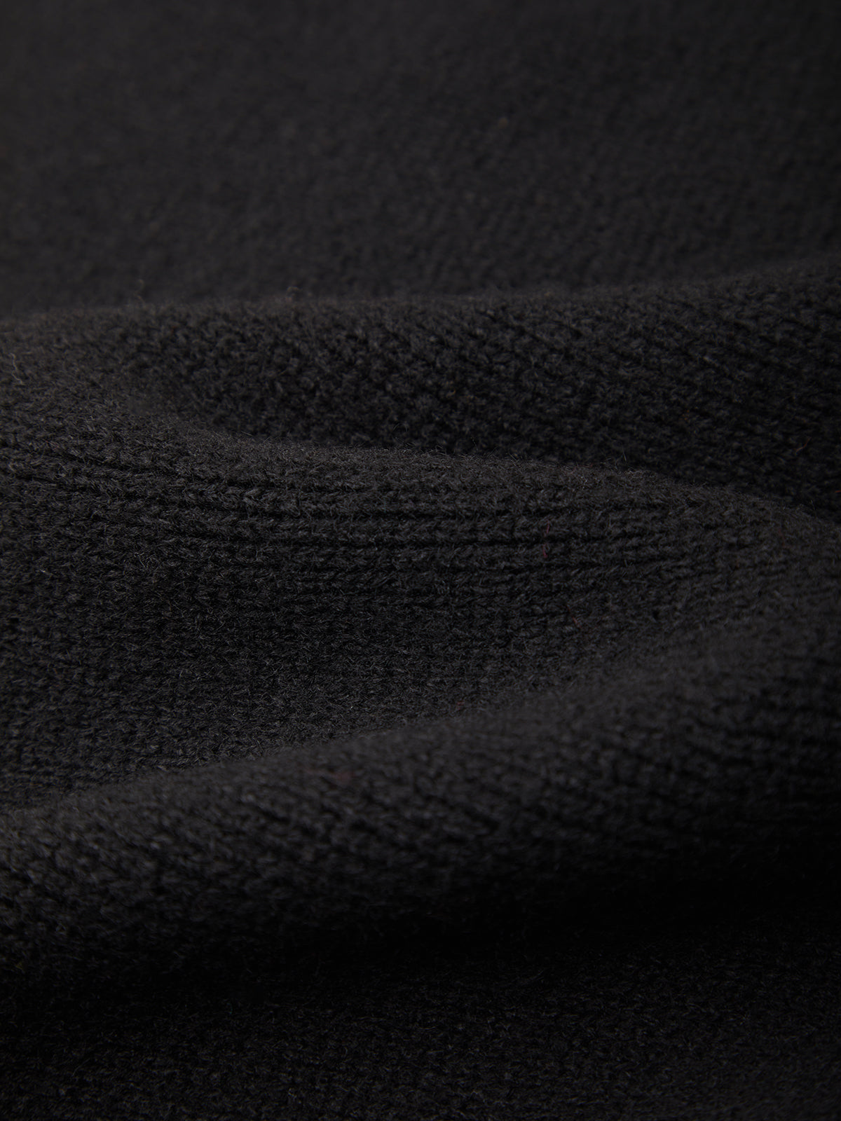 Close-up of a black ribbed knit fabric texture with soft folds and shadows.