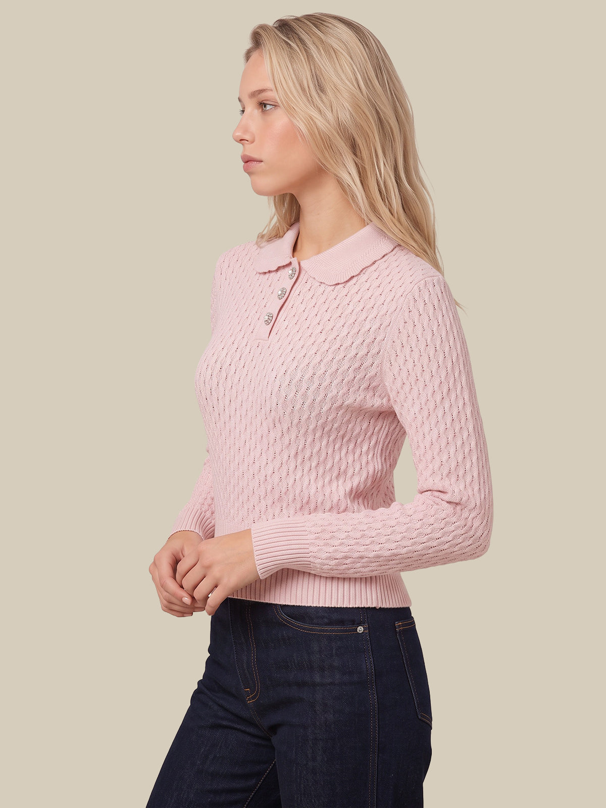 A woman wearing a light pink long-sleeve polo sweater with a textured cable knit pattern and dark blue jeans, shown from a side profile against a solid beige background.