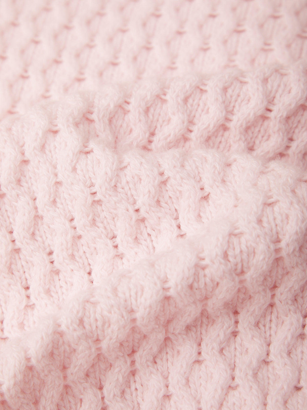 A close-up of a light pink textured knit fabric with a ribbed and cable-knit pattern.