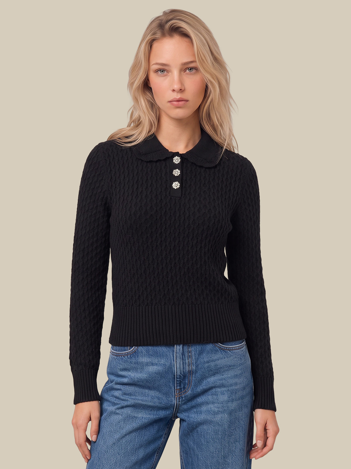 A woman modeling a black cable-knit polo sweater with a three-button collar, paired with blue jeans, against a solid beige background.