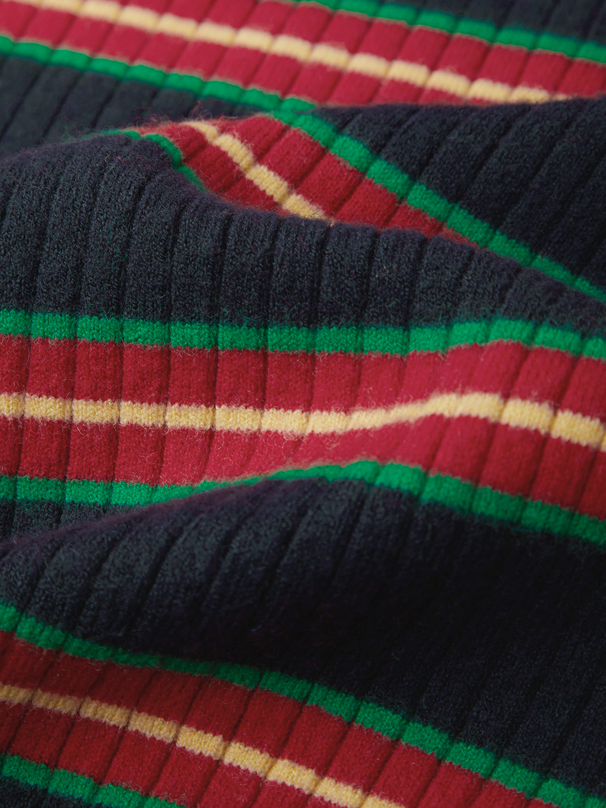 Close-up of a ribbed knit fabric with a striped pattern in dark navy, red, green, and cream.