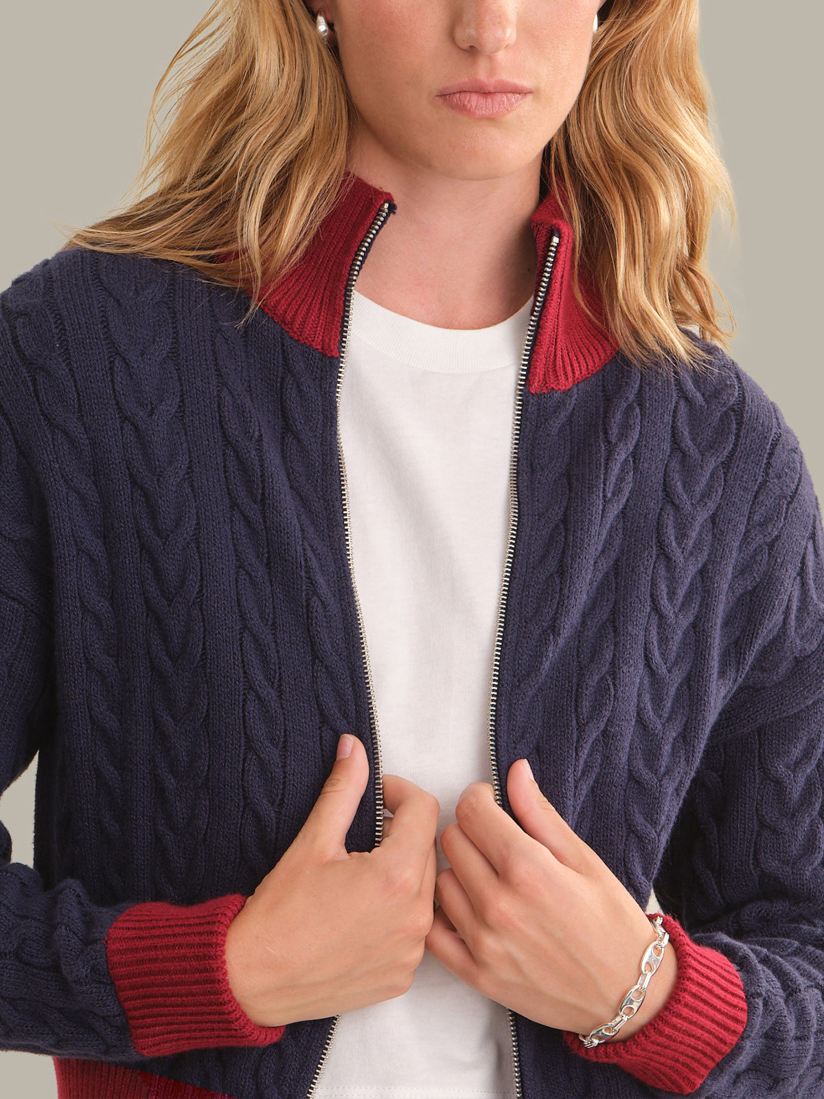 A woman wearing a navy blue cable-knit zip-up sweater with contrasting red ribbed collar, cuffs, and hem, layered over a white t-shirt.