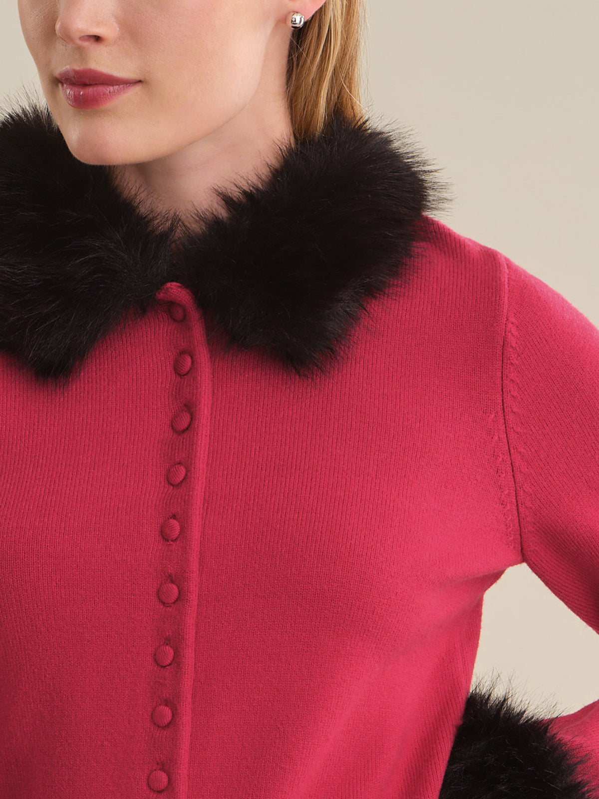 A close-up of a woman wearing a bright pink knit cardigan with a large black faux-fur collar and matching dark buttons down the front.