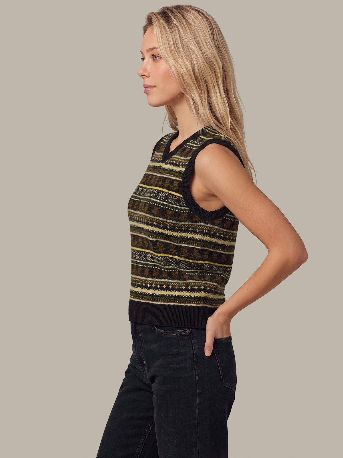 A woman in profile wearing a sleeveless knit top with horizontal geometric patterns in black, olive green, and beige, paired with dark jeans, against a solid light gray background.
