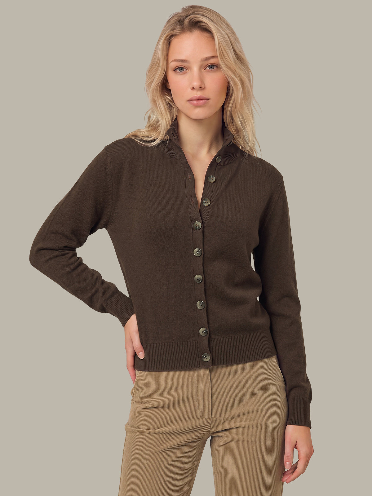 A blonde woman modeling a dark brown button-up knit cardigan sweater with a stand collar, paired with beige pants, against a solid light gray background.