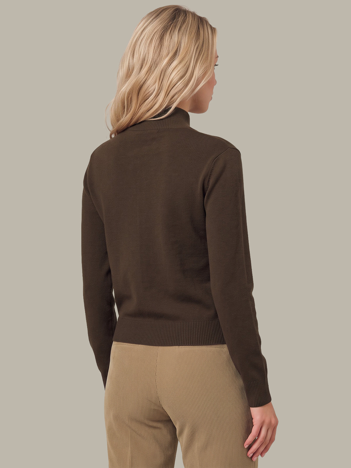 A woman shown from the back wearing a dark brown mock-neck knit sweater and beige pants, set against a solid light gray background.