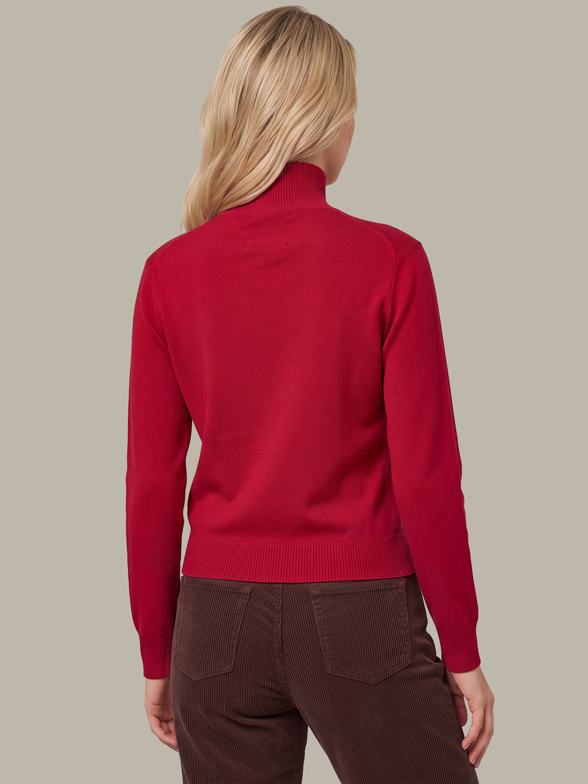 A woman shown from the back wearing a bright red mock neck sweater and dark brown pants, set against a solid light gray background.