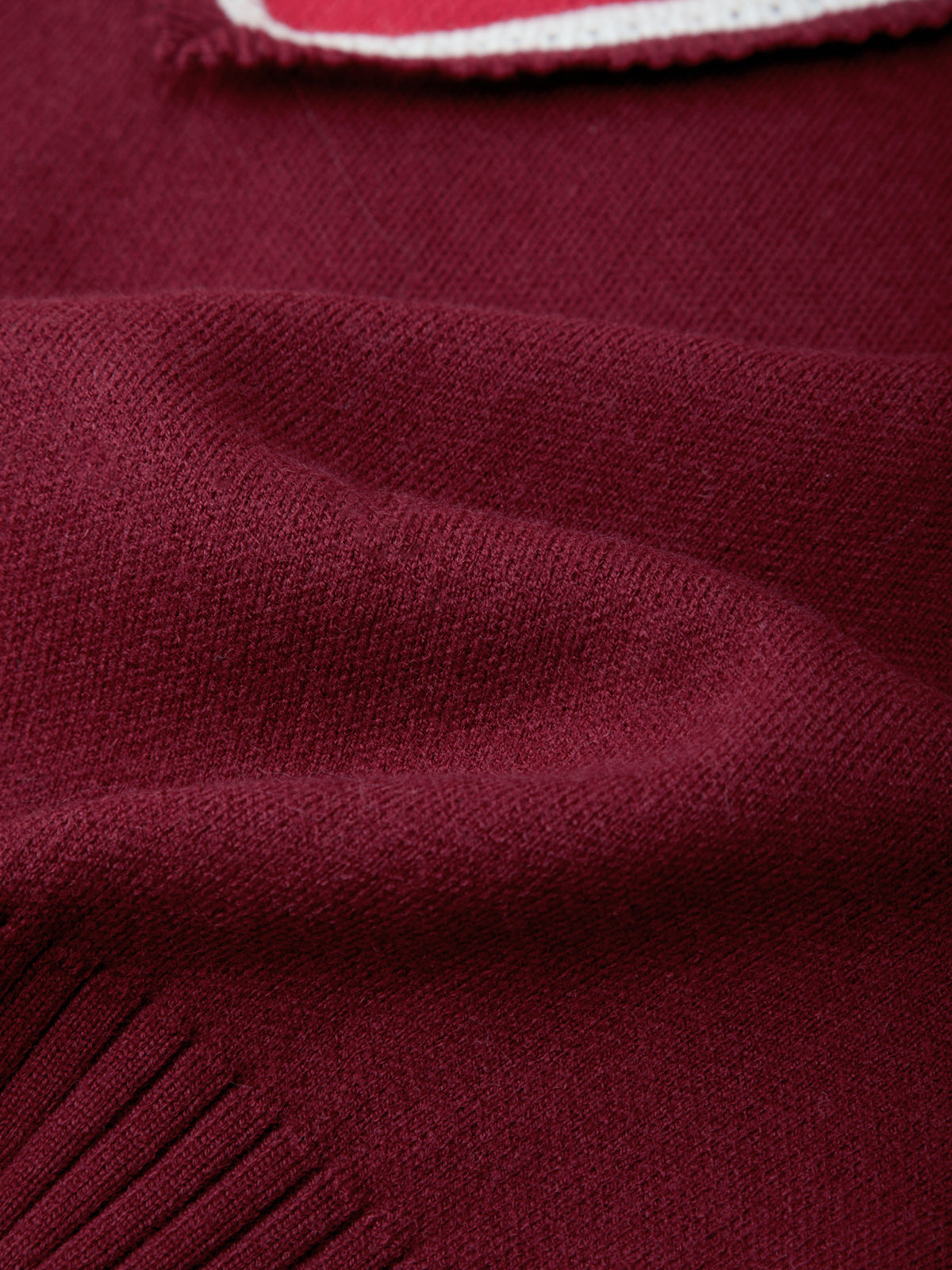Close-up of a burgundy knit fabric texture with a small portion of a white and red striped trim visible at the top edge.