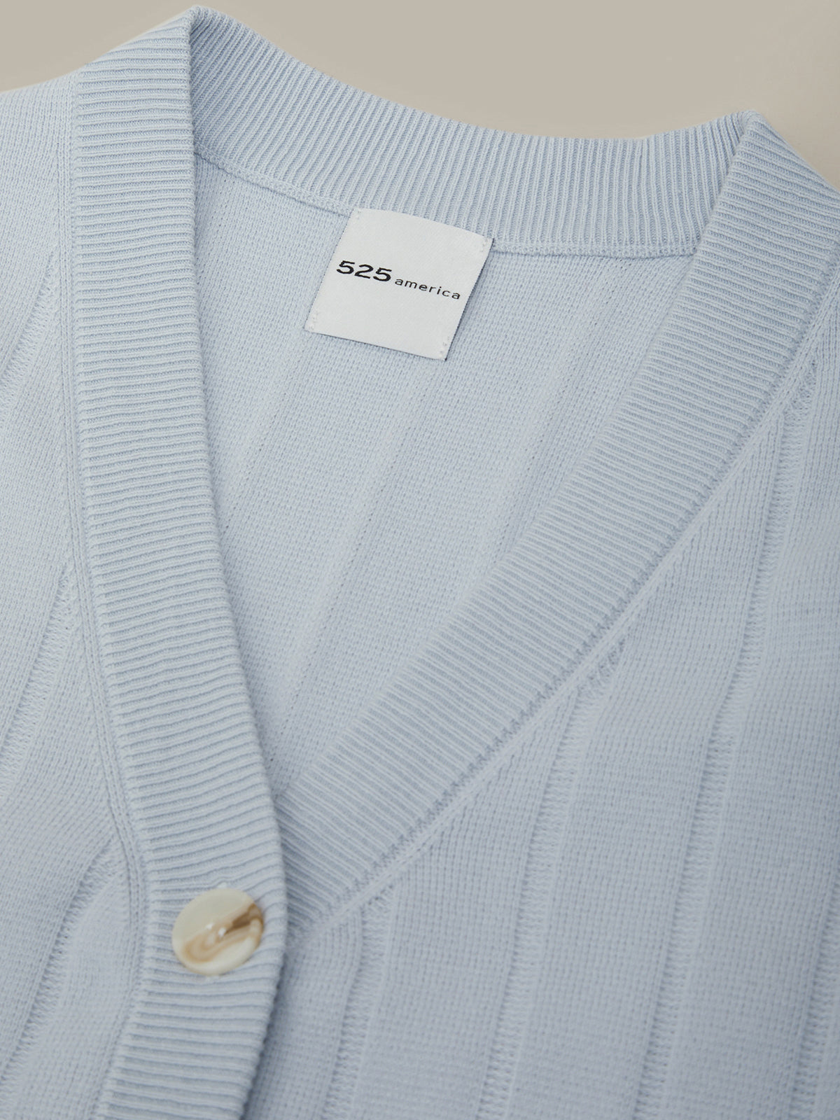 Light blue cardigan with a brand label on a beige background