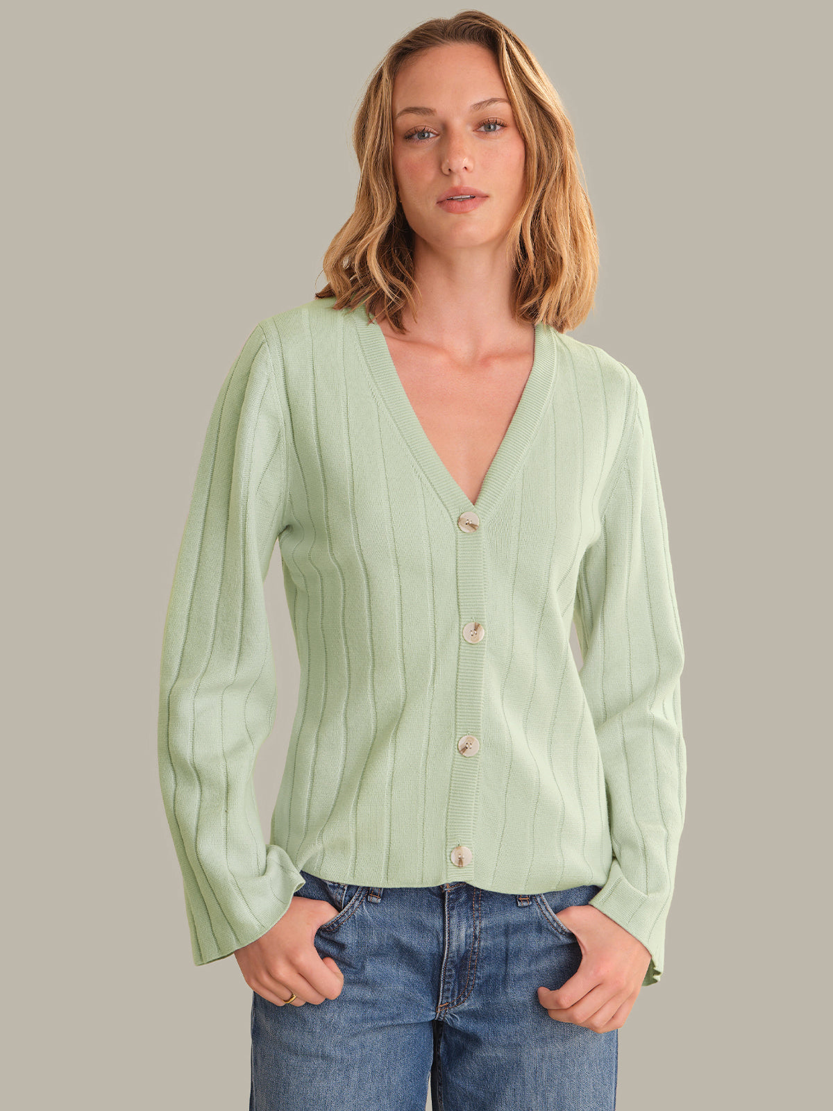 Woman wearing a light green ribbed cardigan with buttons, standing against a plain background