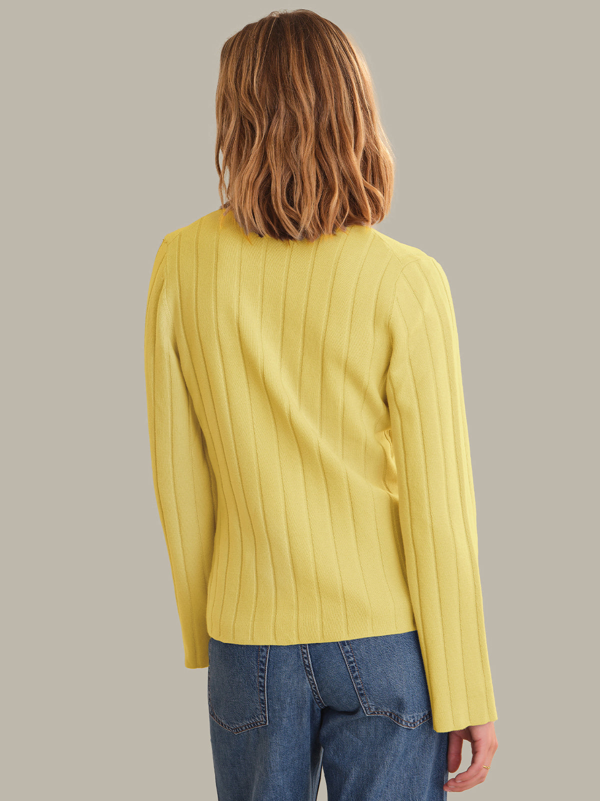 Person wearing a yellow cardigan and blue jeans against a plain background