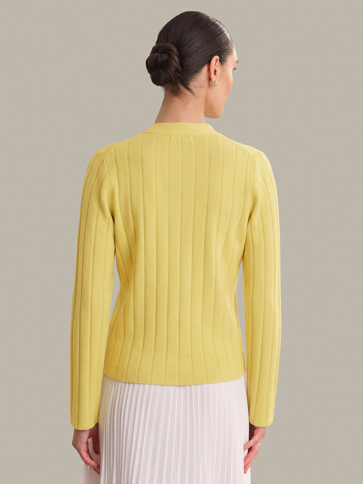 Woman wearing a yellow ribbed sweater against a plain background