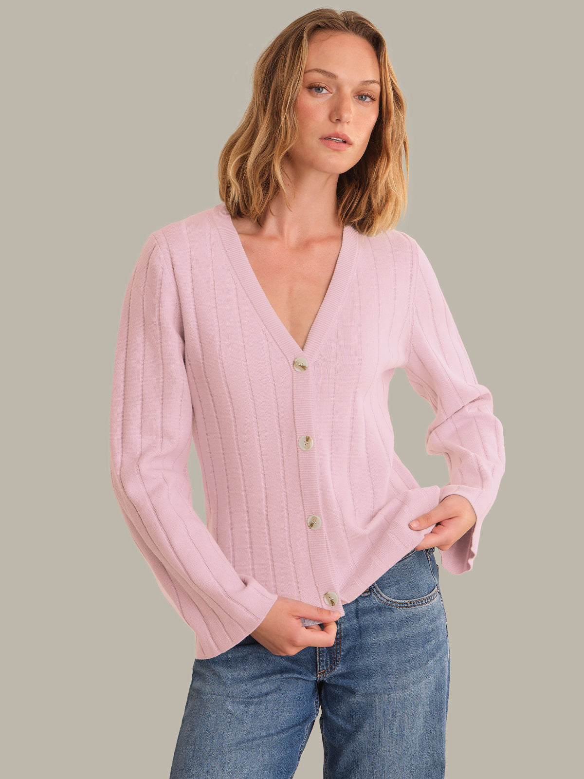 Woman wearing a pink ribbed cardigan with button details against a neutral background