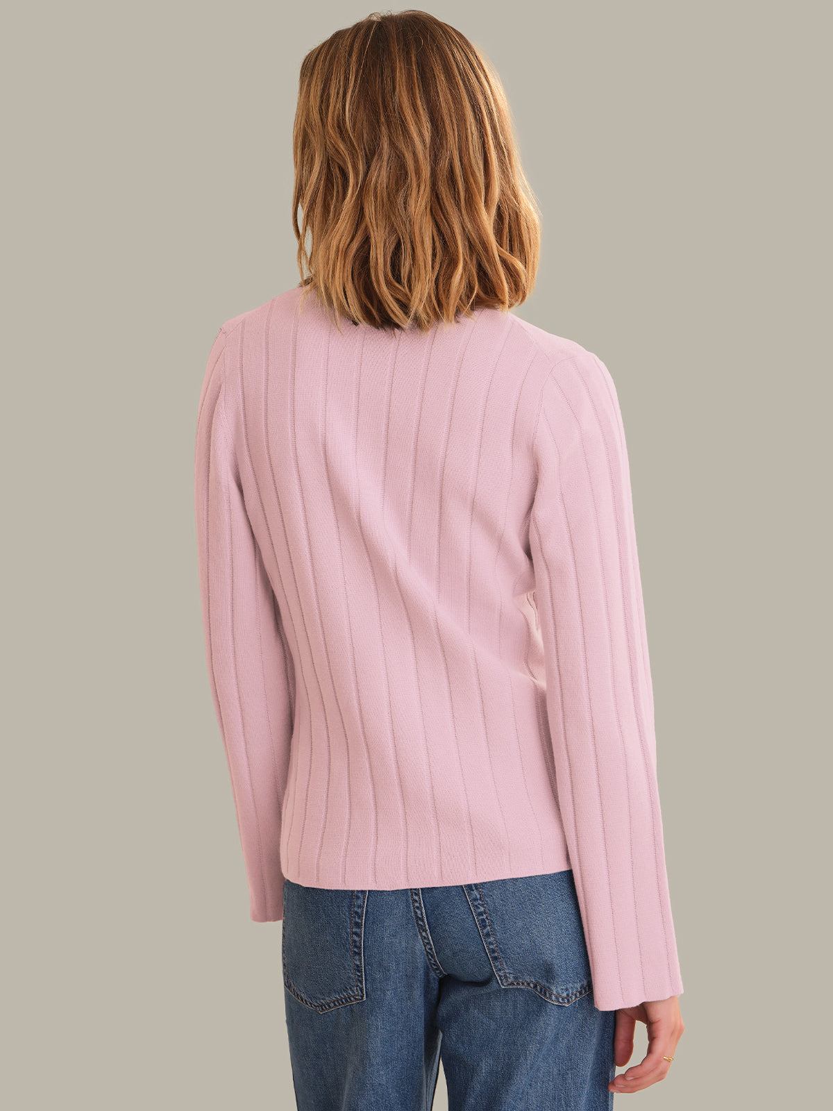 Person wearing a pink cardigan and blue jeans on a plain background