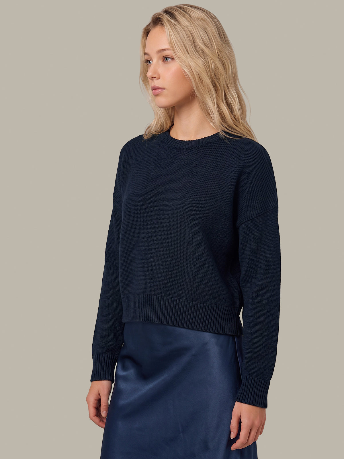 A woman wearing a dark navy blue knit sweater and a matching navy satin skirt, photographed against a solid light gray studio background.