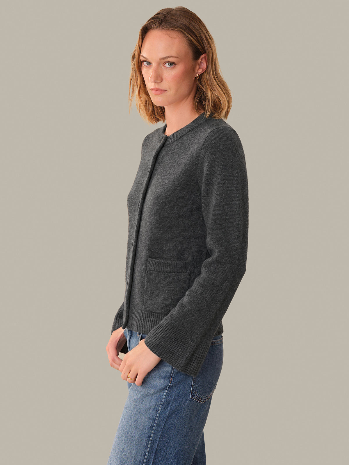Woman wearing a dark gray cardigan and blue jeans against a plain background