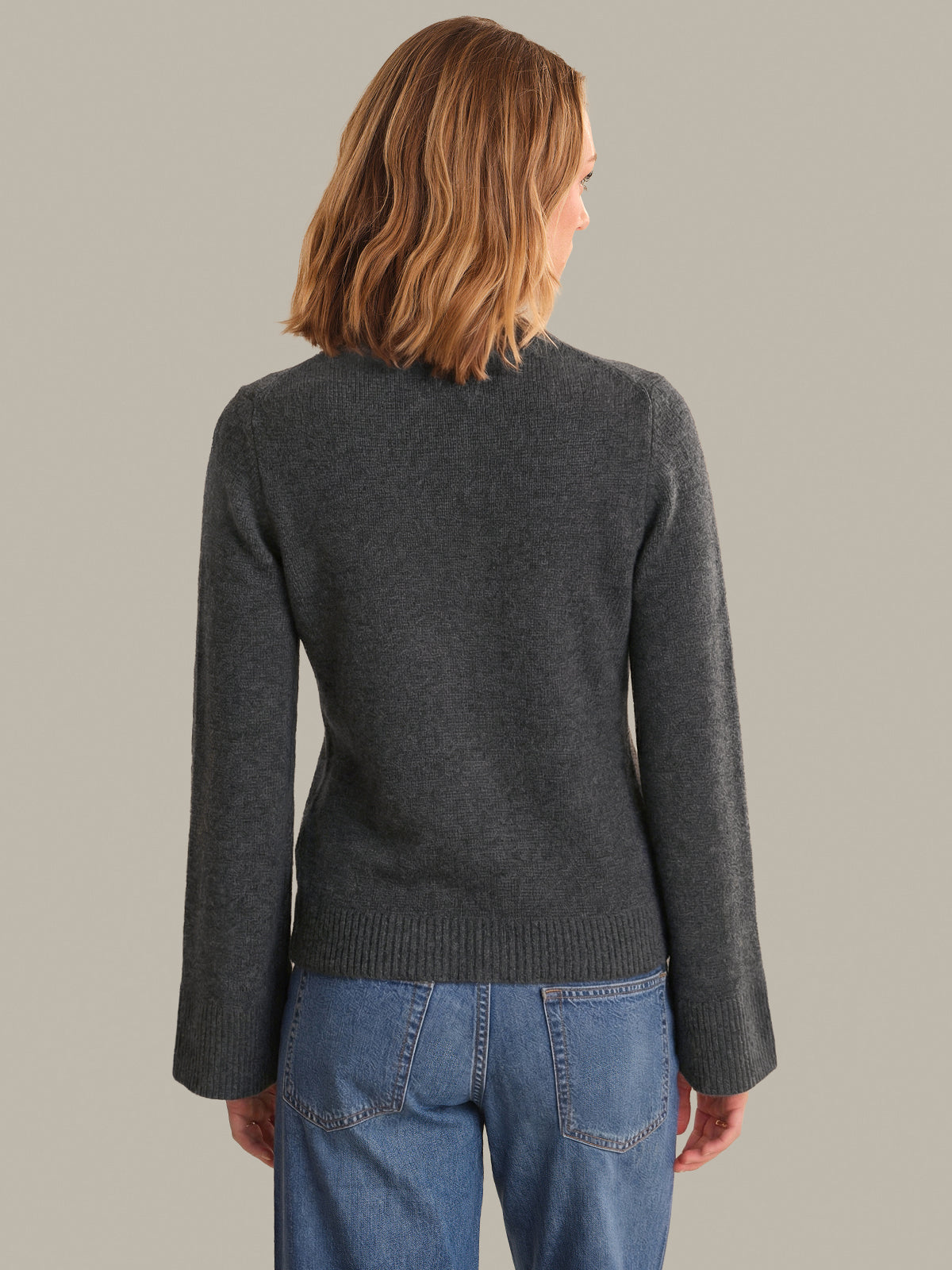 Person wearing a dark gray sweater and blue jeans on a plain background