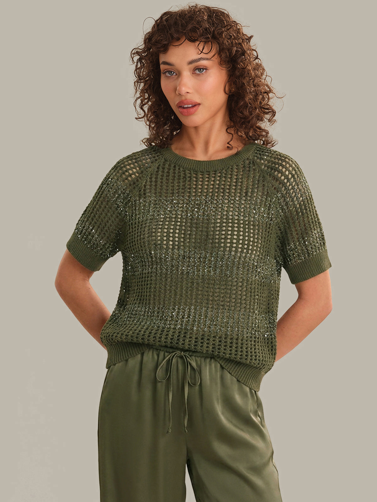 Woman wearing a green knitted top and pants against a neutral background