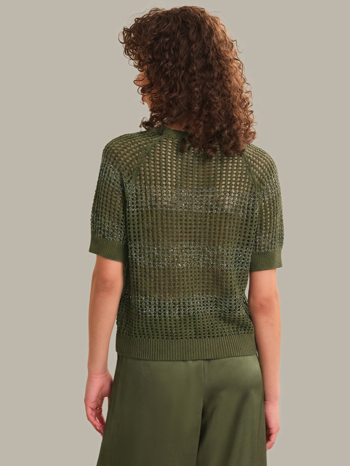 Person wearing a green knitted top and pants against a neutral background